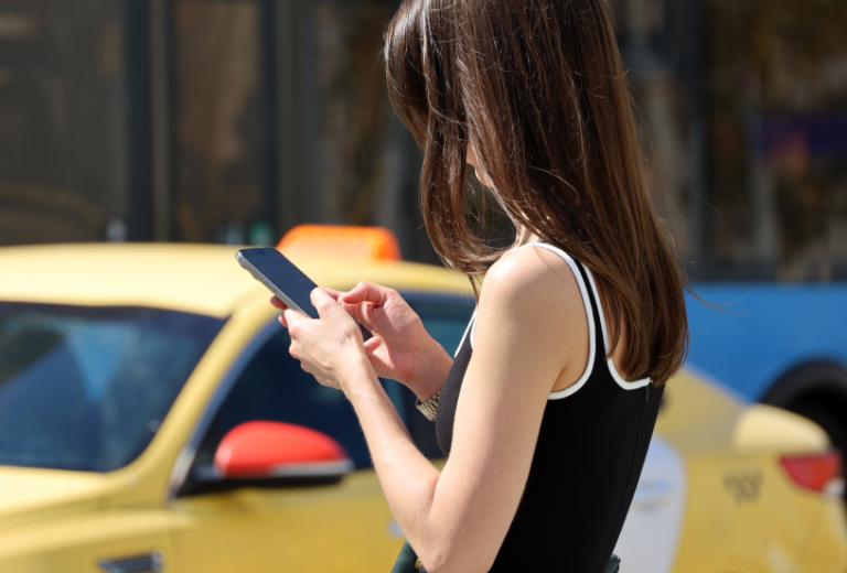 Taxsówka w tle, kobieta zamawia przewóz taxi poprzez aplikacje Bolt
